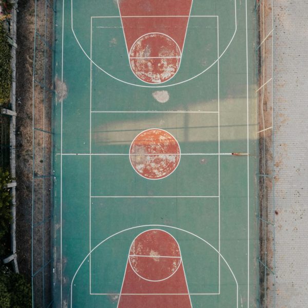 A top-down aerial view of an old outdoor basketball court with worn-out markings.