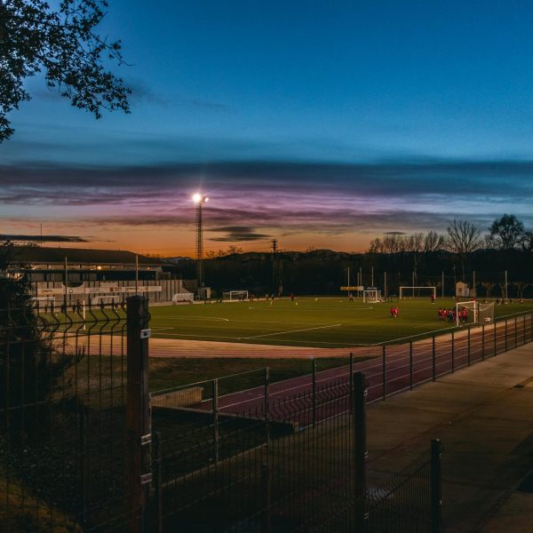 Football field illuminated by stadium lights at dusk with players practicing.