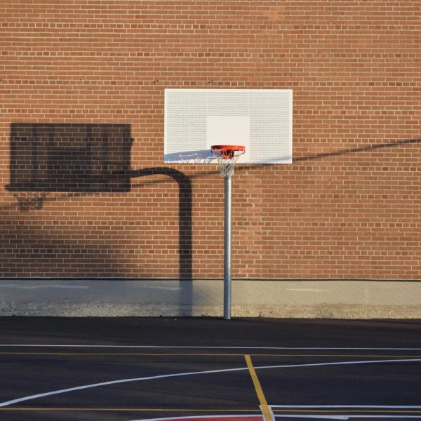 Empty outdoor basketball court with hoop and shadow against brick wall